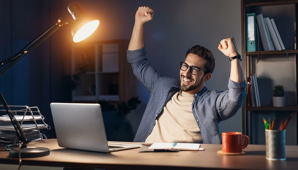 Homem celebrando em frente ao computador após economizar na compra de passagem