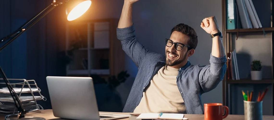Homem celebrando em frente ao computador após economizar na compra de passagem